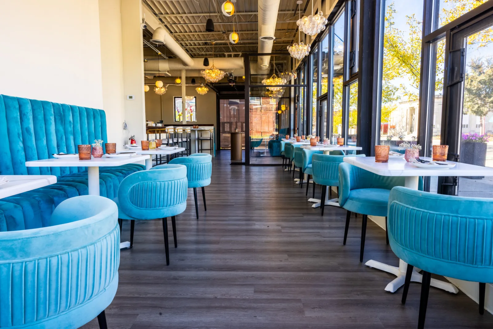 Antidote's sunlit dining room with teal velvet booths, marble tables, and bubble chandeliers